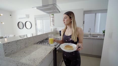 Young-caucasian-blonde-girl-in-sportswear-sitting-in-the-kitchen-of-a-mansion-to-have-healthy-breakfast