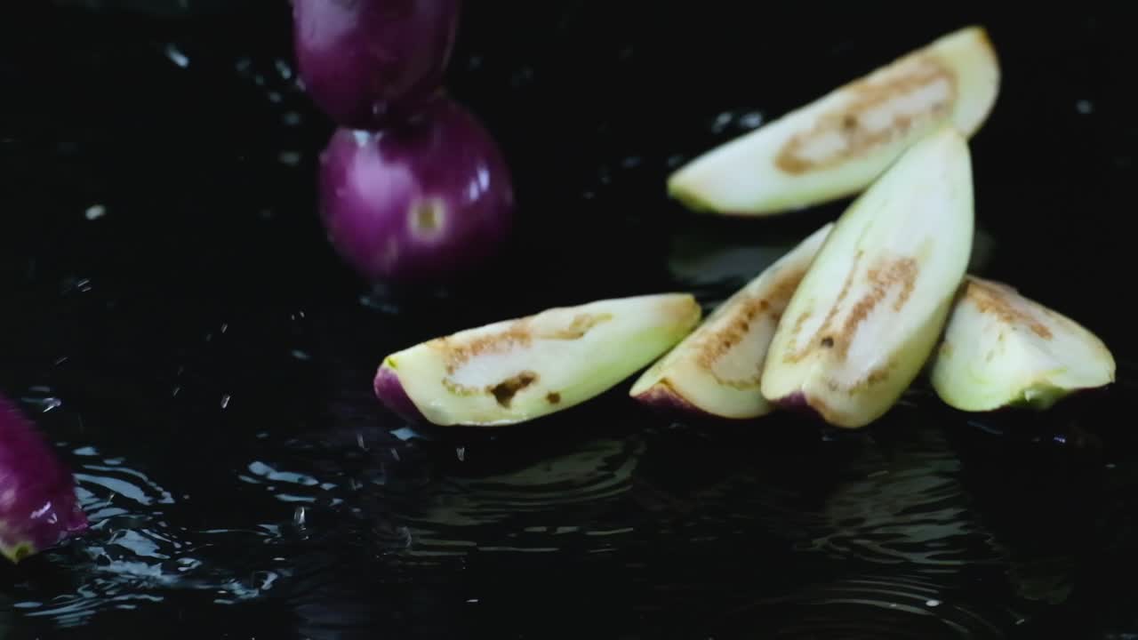 Sliced and Whole Eggplants Fall Down on a Black Background