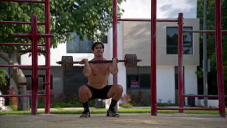 Cámara-Lenta-De-Un-Hispano-Sin-Camisa-Realizando-Dos-Sentadillas-Frontales-En-El-área-De-Fitness-De-Un-Parque-Local-En-México