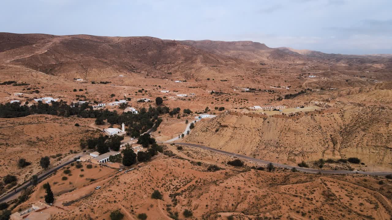 Vista aérea de Ksar Hallouf, Tunísia. Edifícios brancos aninhados entre palmeiras em uma paisagem seca e montanhosa