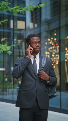 vertical video shot of smiling young businessman wearing suit using mobile phone walking outside past offices in the financial district of the city of london uk shot in real time