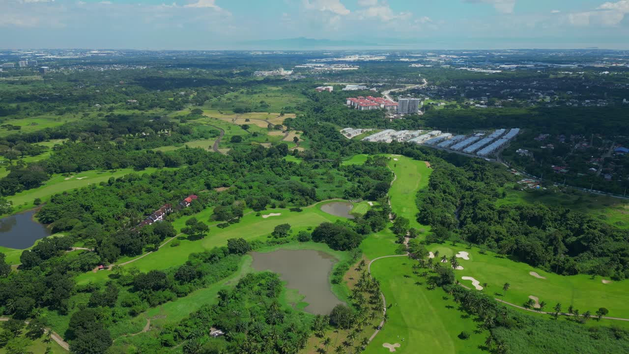 A push aerial moving across manicured fairways and tropical greenery, gradually revealing the distant horizon and urban skyline blending with natural landscapes in Calamba Laguna, Philippines