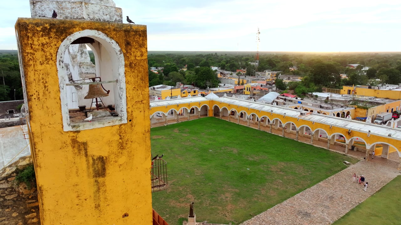 Vista aerea di un angolo del grande porticato giallo e dell'atrio del convento di Sant'Antonio a Izamal, Yucatán, Messico, con archi che fiancheggiano il cortile verde