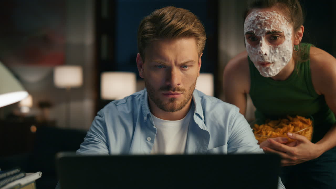 Focused guy reading device evening flat closeup. Woman eating pointing computer