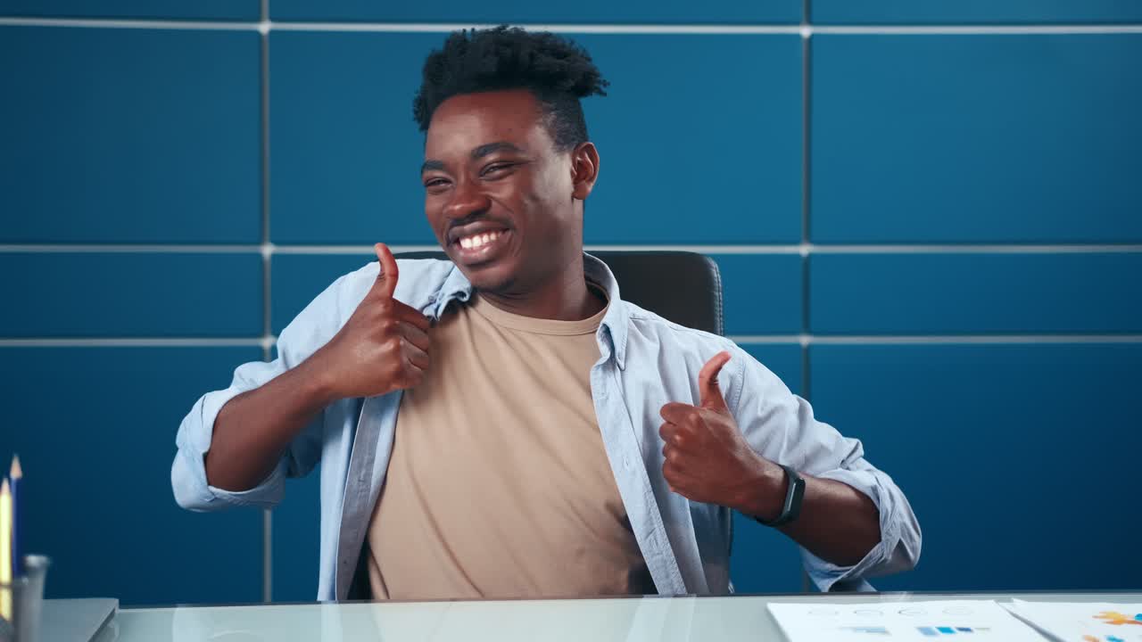 Ritratto di uomo afroamericano soddisfatto che mostra il pollice in su con entrambe le mani in ufficio.