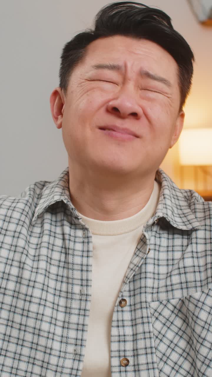 화가 난 중국인 남자가 집에서 소파에서 tv를 보는 결과에 실망한 얼굴을 하고 있습니다.