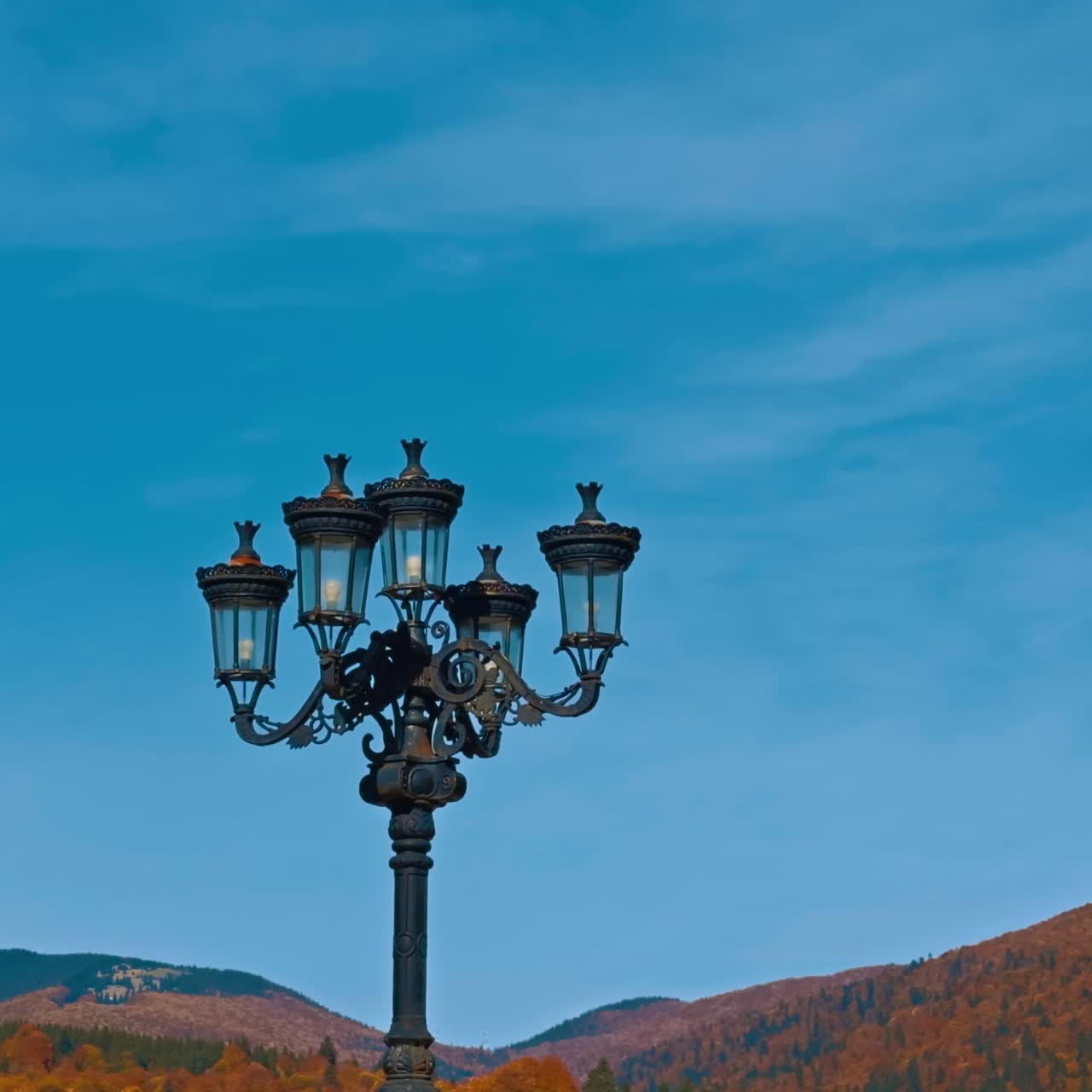Due lampioni neri in stile antico. Visuale dal basso. Montagne sullo sfondo in una soleggiata giornata autunnale