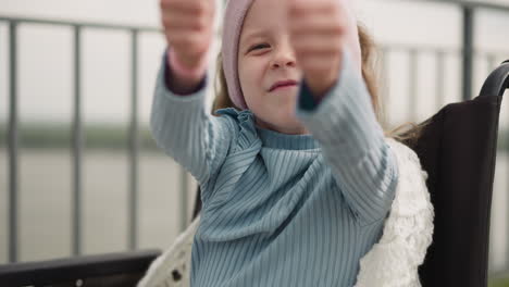 cheerful girl shows thumbs up gesture sitting in wheelchair