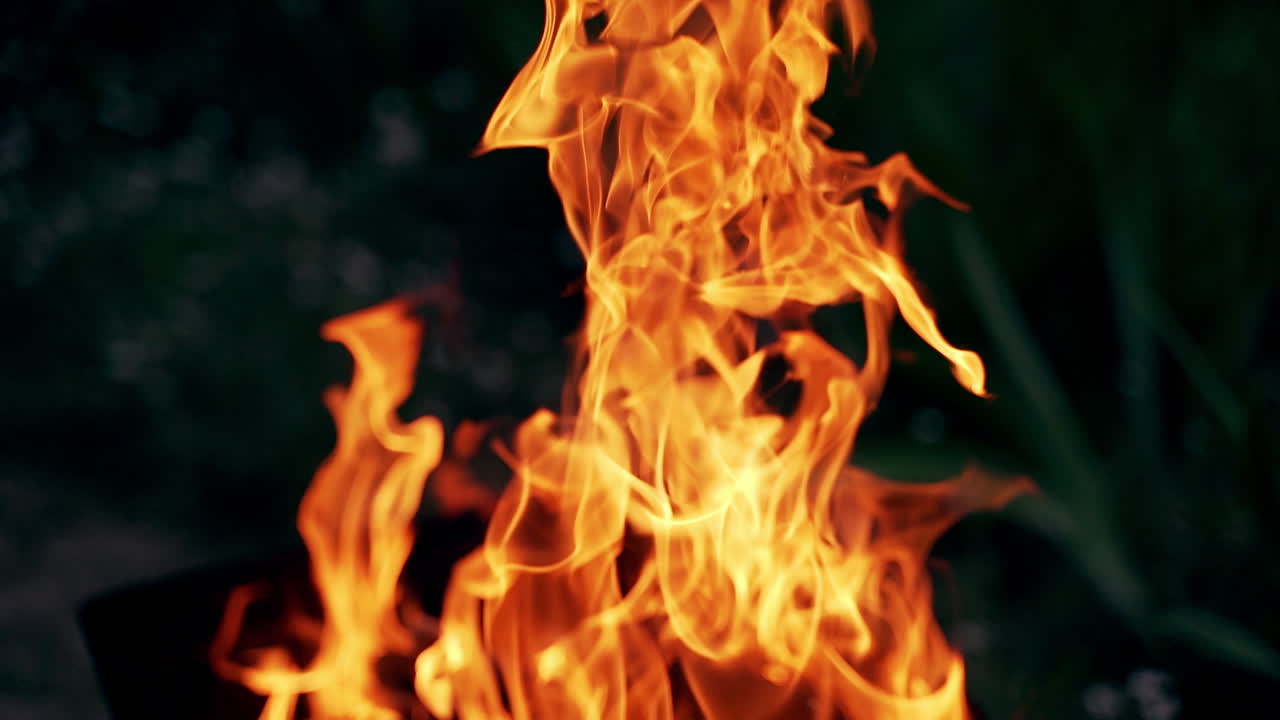 Beautiful bright flame on dark background. Romantic atmosphere of burning firewood at night. Orange flame outdoors.