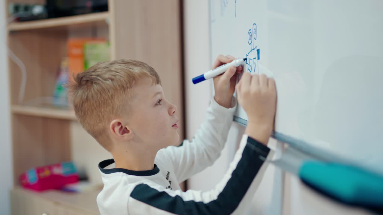 Schoolboy draws on white blackboard. Side view of a little boy writing with a marker on magnetic board in the classroom. Elementary education.