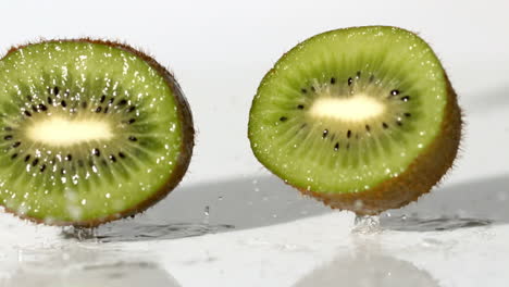las mitades de kiwi cayendo sobre un fondo blanco húmedo