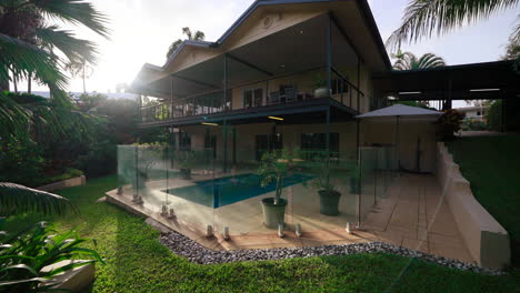 pullback from backlit large tropical home house with pool in backyard of luxurious gathering area patio and balcony