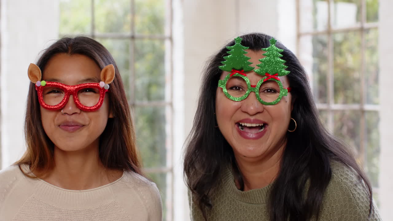 At christmas, asian grandmother and granddaughter wearing festive glasses laughing and enjoying than