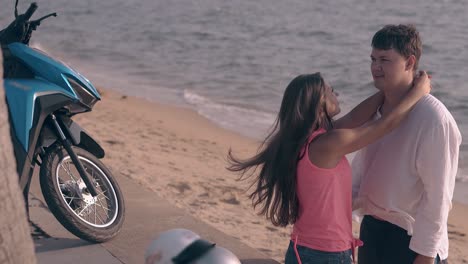 girl-hugs-handsome-tall-man-on-beach-against-blue-ocean