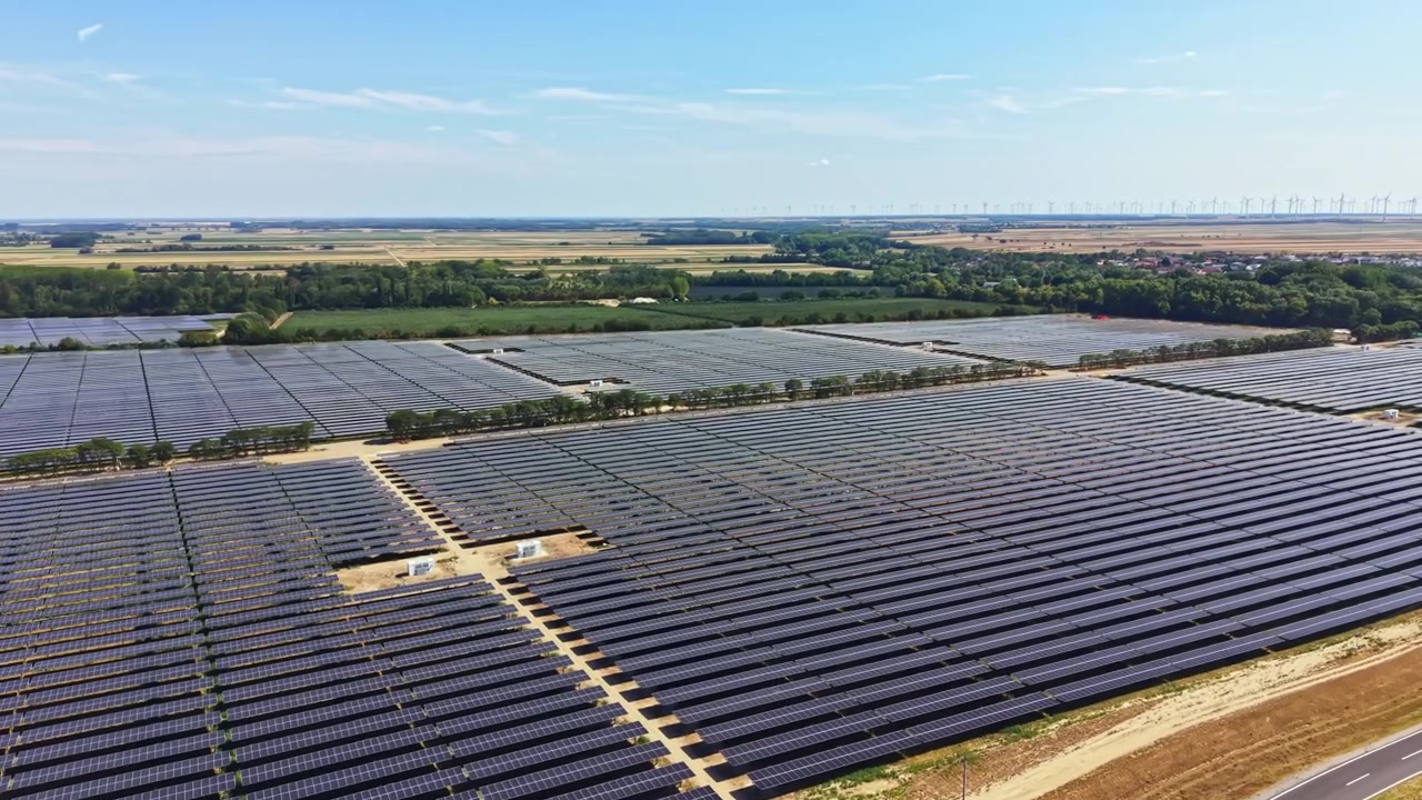 Stor solcellepark beliggende i et landområde med rækker af solpaneler under en klar blå himmel om dagen