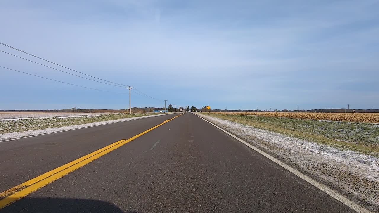 Point of View out of the drivers window; Driving on highway past farms, truck and corn fields in rural Illinois USA on snow and ice.
