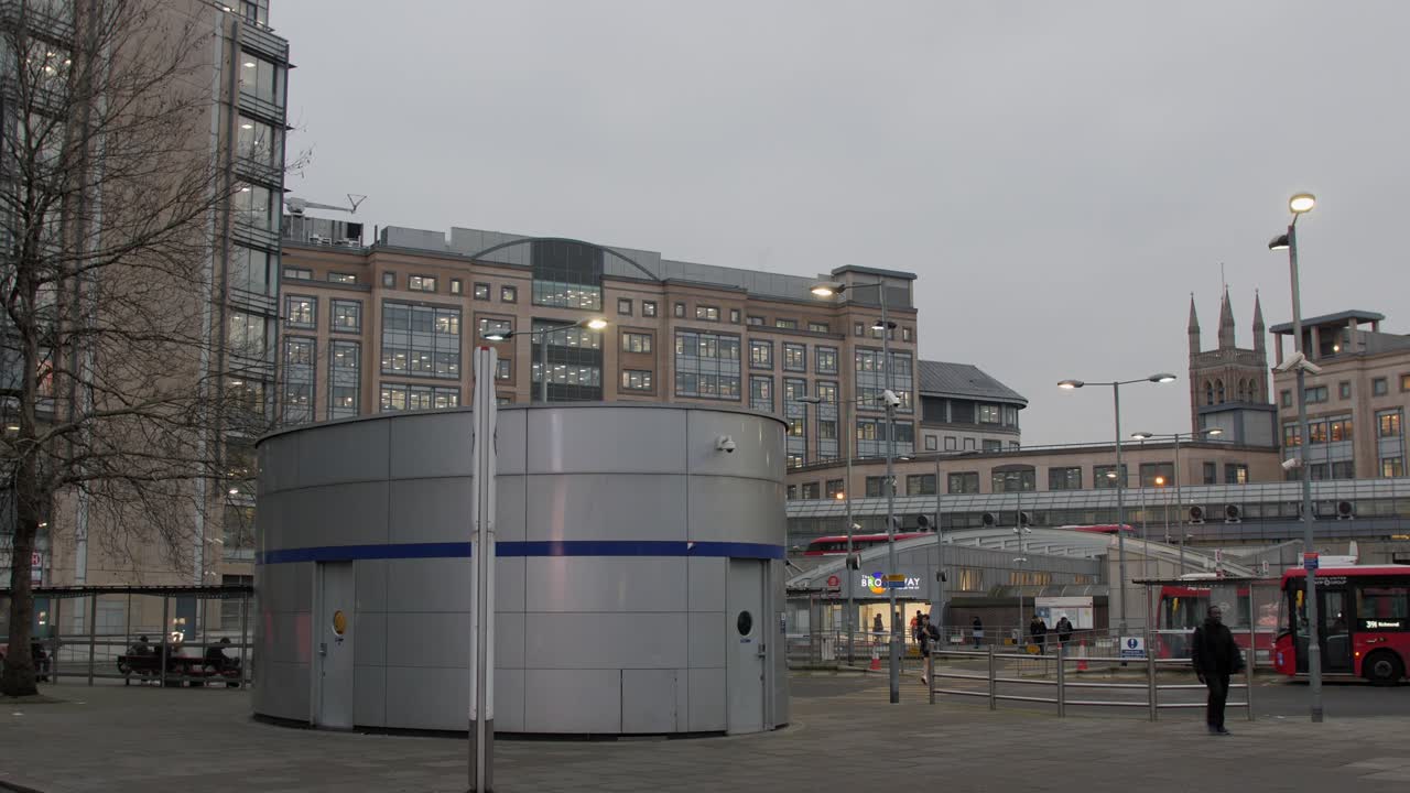 Handheld shot of Hammersmith bus station with surrounding modern buildings at dusk