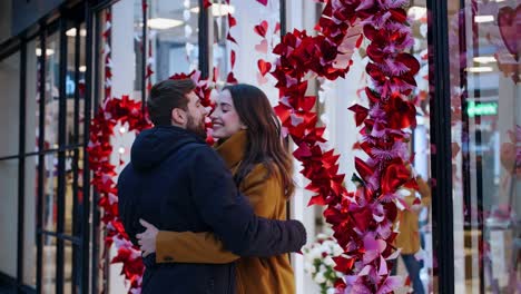 romantic couple sharing loving embrace near shop window, adorned with heart shaped butterflies in vibrant red and pink hues, expressing tender connection