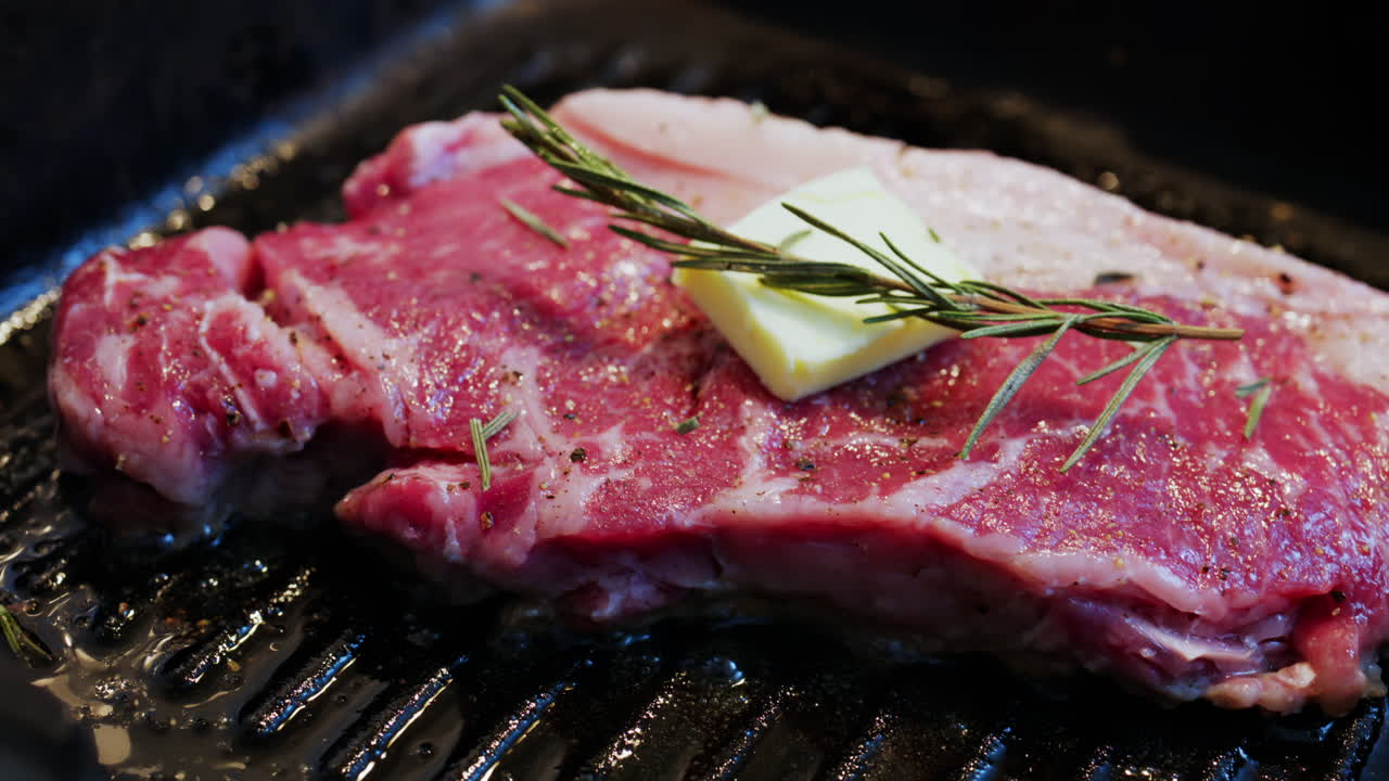 Burro che si scioglie su una bistecca condita che cuoce su una padella griglia calda con rosmarino