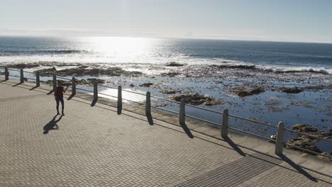 African-american-woman-wearing-backpack-and-walking-on-promenade-by-the-sea