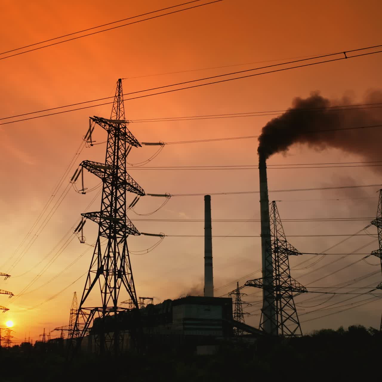 Environment in danger. Thick harmful smoke released from pipe into the sky among high-voltage electric towers against red dramatic sky at sunset