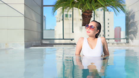 asian woman in her 30th relaxing in luxury rooftop outdoor swimming pool at bangkok city hotel