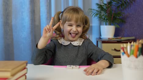 niña mirando una cámara web haciendo una llamada de video, estudiando lecciones en casa, sonriendo mostrando la lengua