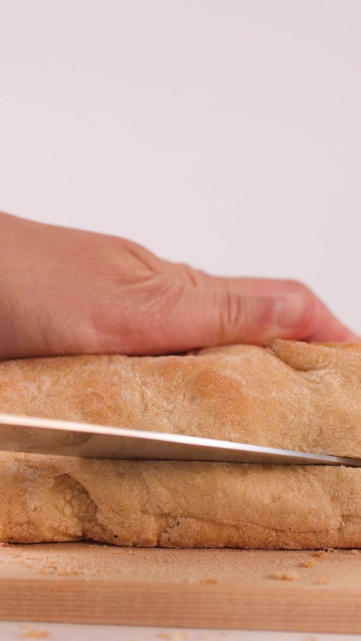 Close-up shot of hands using a knife to slice fresh sourdough bread on wood.