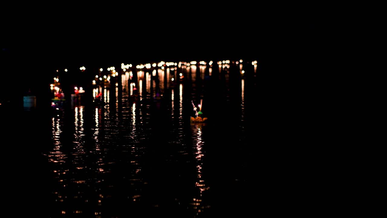krathong flotando en un arroyo en la oscuridad a medida que avanza hacia más luces de velas flotantes que se reúnen en el otro extremo del arroyo durante loi krathong en tailandia