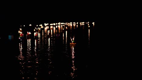 krathong floating on a stream in the dark as it moves towards more floating candlelights gathering at the far end of the stream during loi krathong in thailand