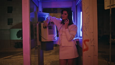 young brunette calling telephone correcting makeup in neon call box at night