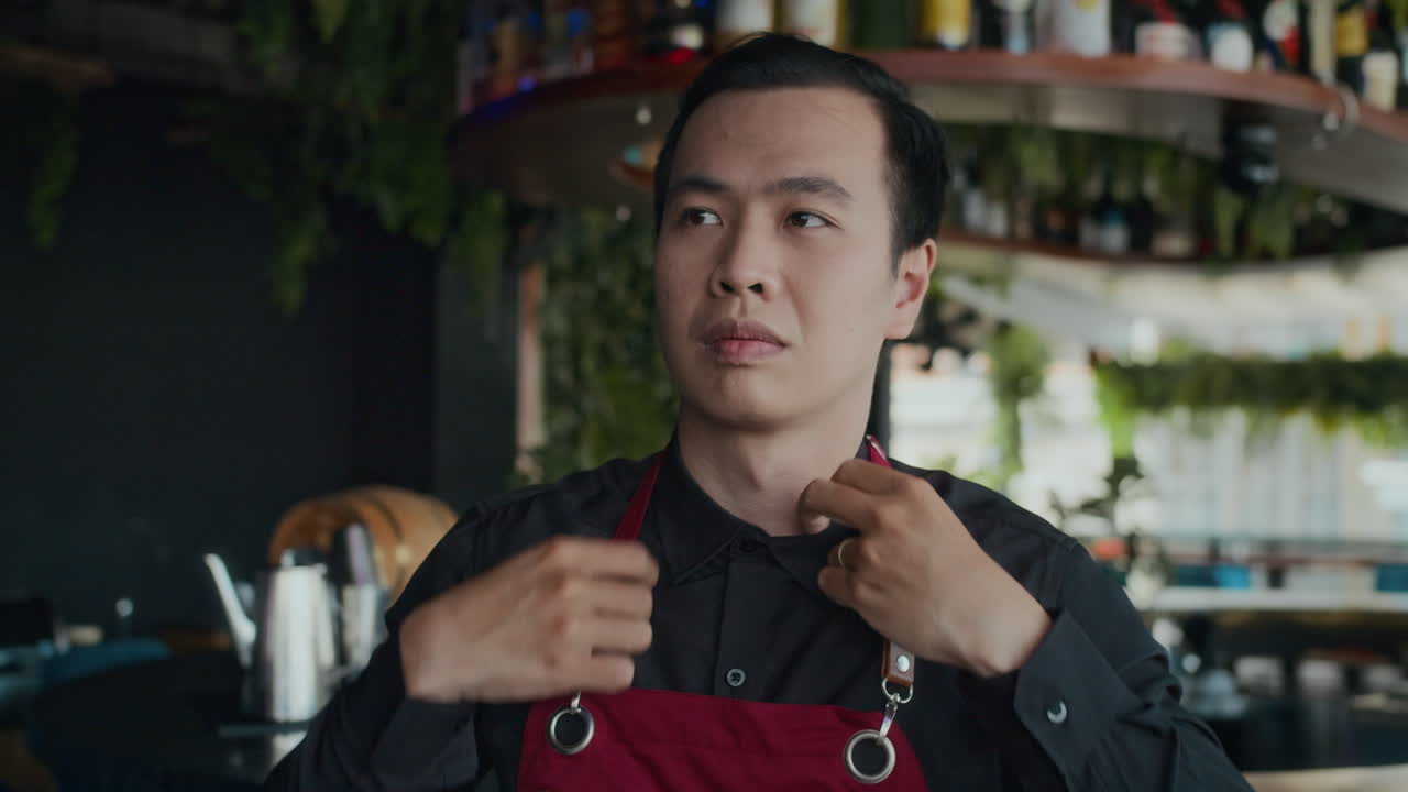 Serious Male Barman Putting on Apron before Work in Restaurant