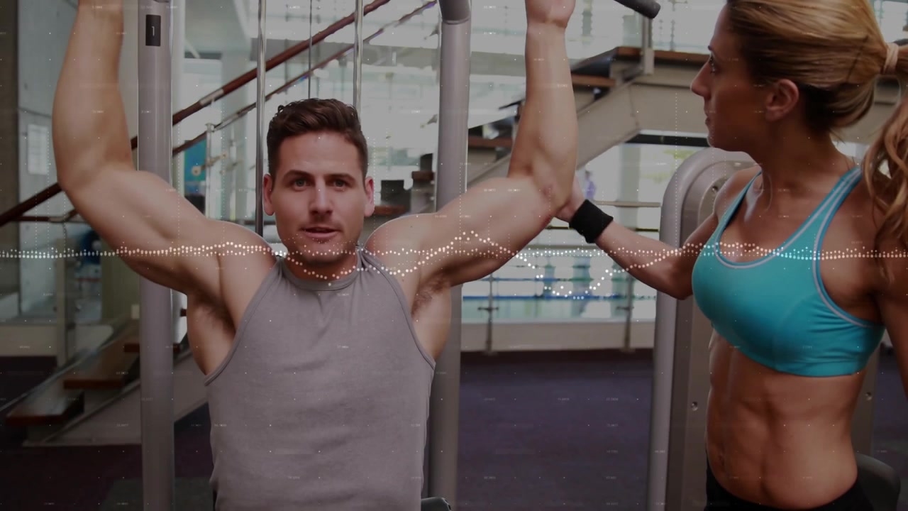 Man pakt een brede lat pulldown stang vast, met een trainer die de houding begeleidt tijdens het uitvoeren van een lat pulldown fitnessoefening.