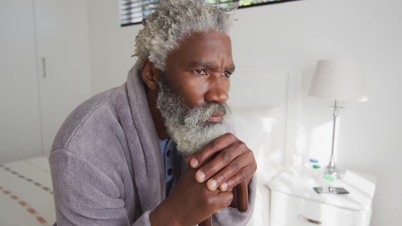 Senior man holding his walking stick while sitting on bed at home