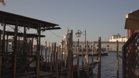 dynamic wide shot of red venetian flag in wind and gondolas parked in pier with wooden poles