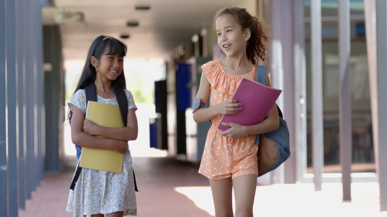 Two biracial girls with backpacks stand in a school corridor