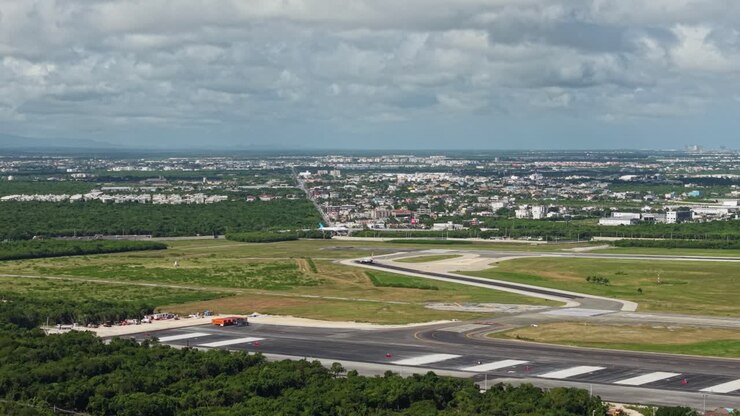 Brede luchtfoto van een passagiersvliegtuig dat landt op de landingsbaan van de luchthaven van Punta Cana. Tropisch landschap, voorstedelijke infrastructuur en blauwe lucht in de Dominicaanse Republiek.