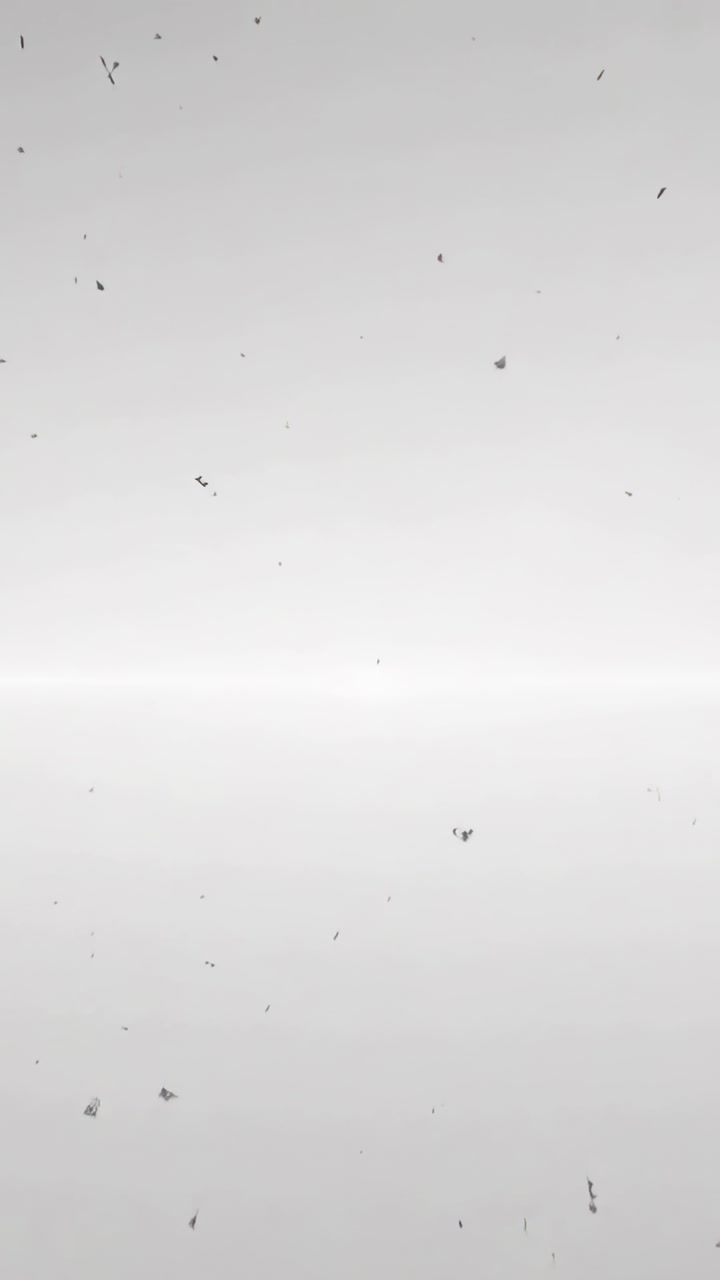 Vertical video: Drifting dark specks and clumps descending over gray backdrop, pulled by gravity