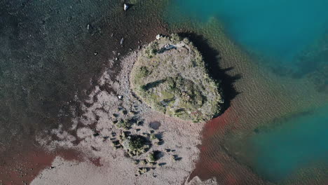 Zoom-out-aerial-view-revealing-a-majestic-natural-lake,-low-vegetation-on-lake-shores,-turquoise-blue-water,-untouched-nature-concept