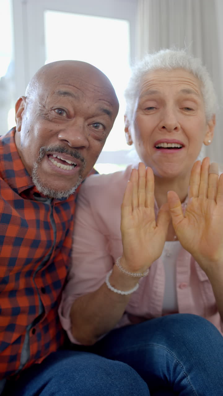 Vertical video of portrait of happy senior biracial couple having video call at home, slow motion