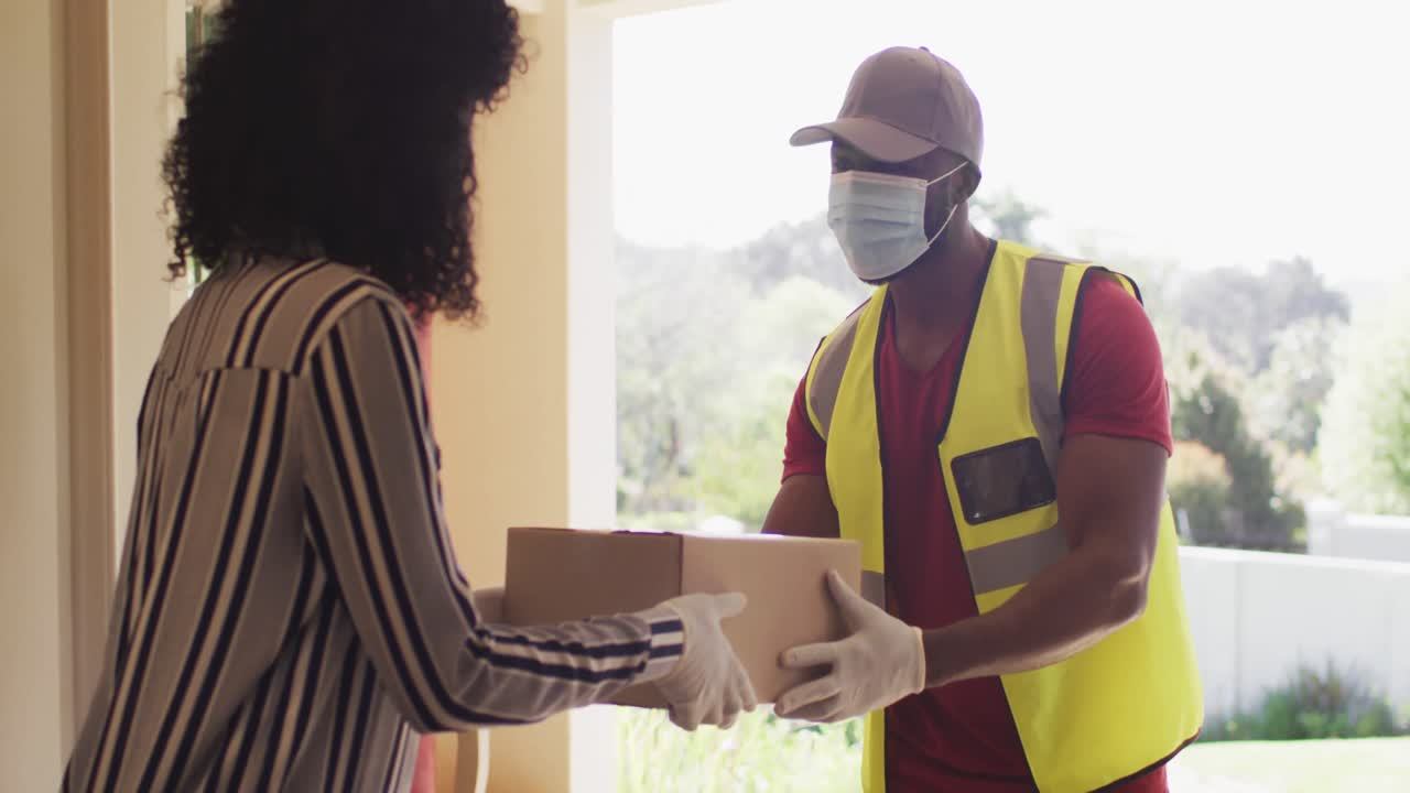 Delivery man wearing face mask delivering package to african american woman wearing face mask at hom