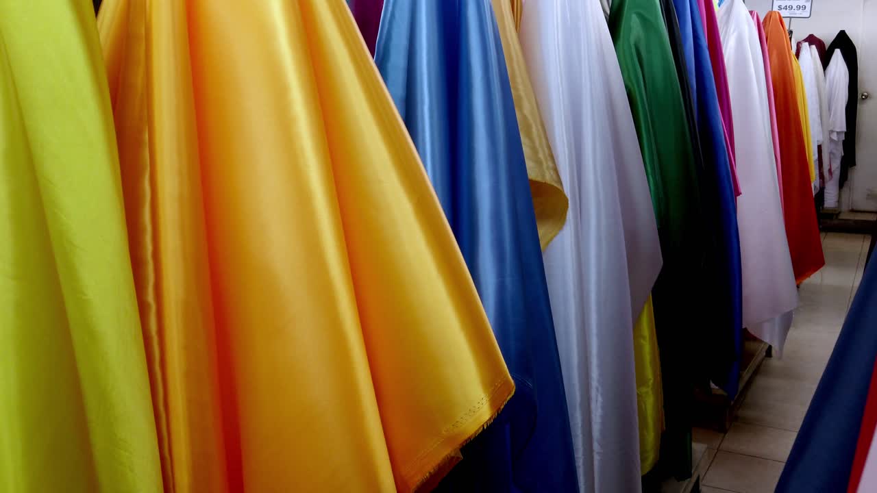 Bright rolls of colorful fabrics on display inside a textile shop. Pan right across vibrant colors under soft indoor lighting
