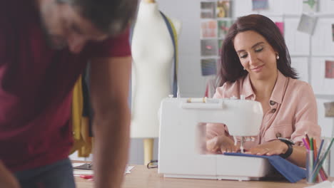 diseñadores de moda masculinos y femeninos con máquina de coser trabajando juntos en el estudio