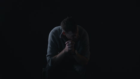 depressed man sits in darkness shaking head