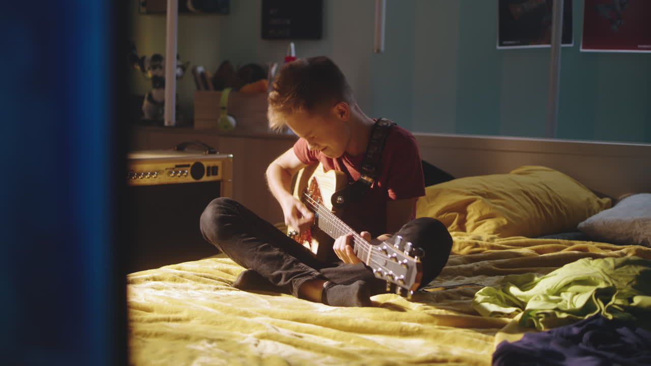침실에서 기타를 연주하는 십대 소년
