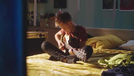 niño adolescente tocando la guitarra en el dormitorio