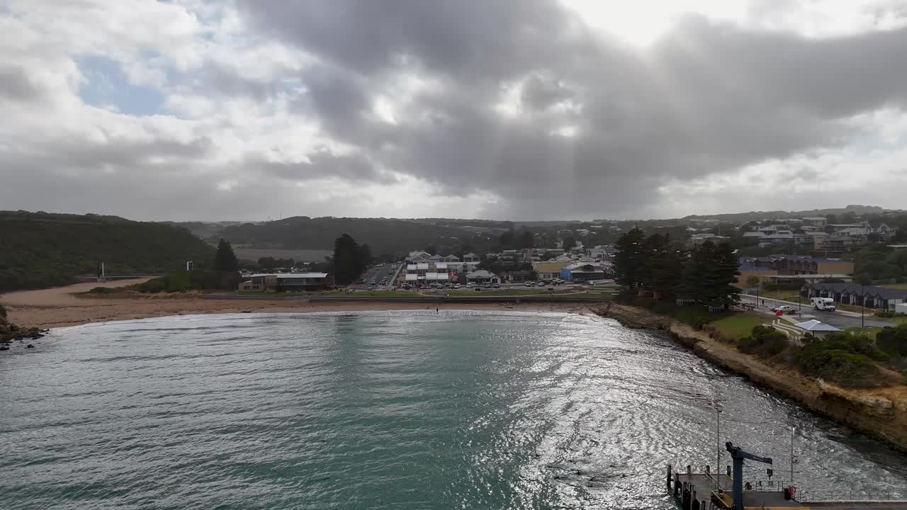 Drone captures Port Campbell's coastal town and pier under dramatic skies, showcasing natural beauty and rural charm