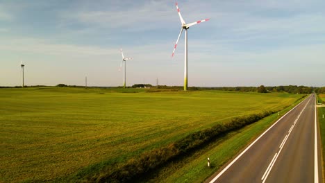 drone shot of a few wind turbines working and generating green electric energy on a wide green field on a sunny day, use of renewable resources of energy, zoom out