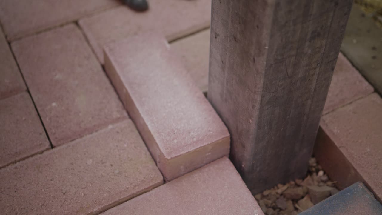 Close-up Worker places paving stone with rubber mallet around a concrete post during outdoor construction landscaping project