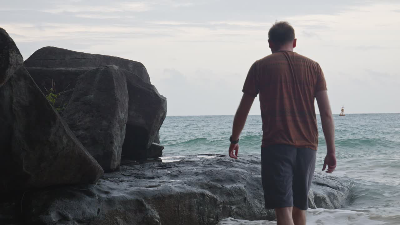 olas ásperas en las rocas con un hombre acercándose a la playa de dam trau, isla de con dao, vietnam